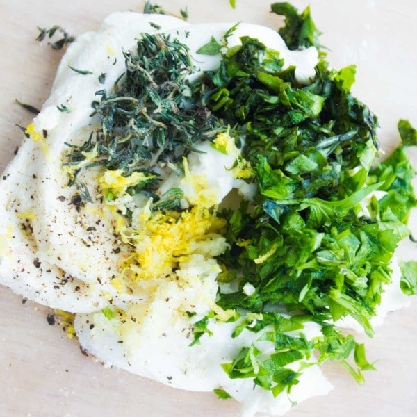 Cream cheese softened and topped with fresh herbs chopped, lemon zest and garlic ready to be mixed.