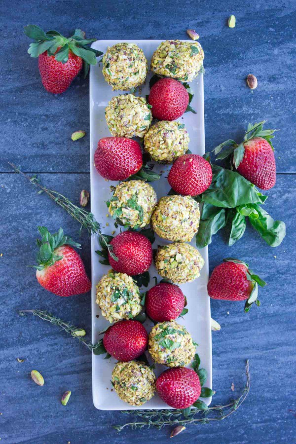 Overhead shot Goat Cheese Pistachio Covered Strawberries lined up on a rectangular white plate placed on a dark wood table.