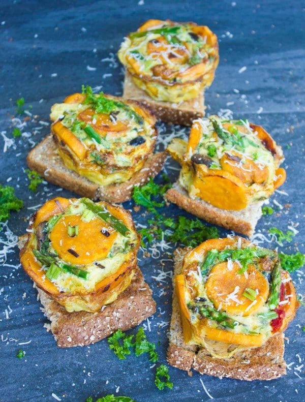 Close-up of a Kale Overhead shot of 5 Veggie Mini Frittatas served on slices of toasted whole wheat bread and sprinkled with Parmesan and chopped kale.