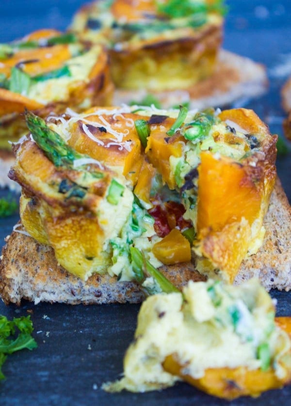 close-up of Kale Veggie Mini Frittatas with one wedge missing placed on a slice of whole wheat toast with more mini-frittatas in the background