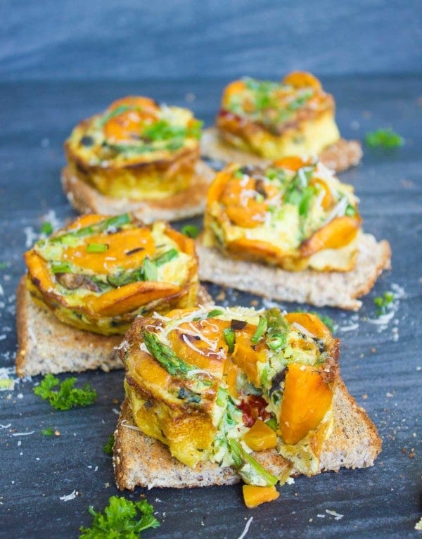 Kale Veggie Mini Frittata with one wedge missing placed on a slice of whole wheat toast with more mini-frittatas in the background