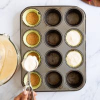 Cheesecake batter being scooped over the cookie bottoms in the baking pan