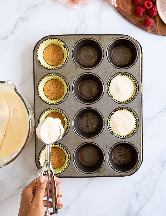 Cheesecake batter being scooped over the cookie bottoms in the baking pan