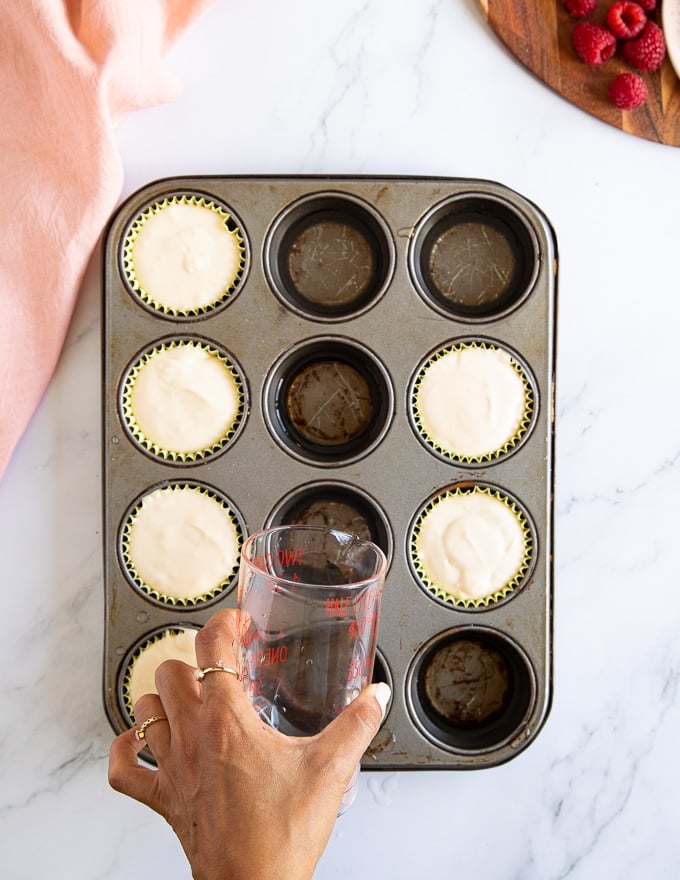 A hand pouring hot water to fill the empty muffin tin cavities