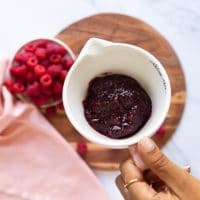 a hand holding a cup of raspberry jam