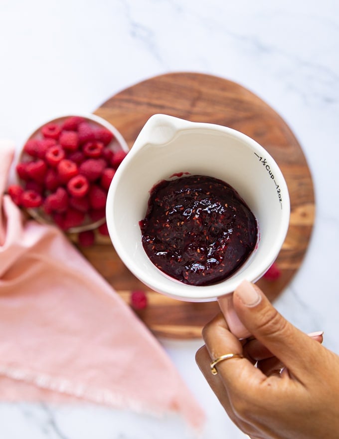 a hand holding a cup of raspberry jam