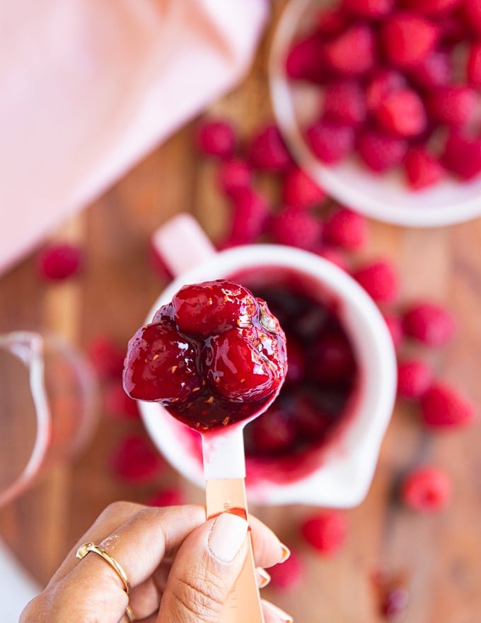 a hand holding a spoon showing off the easy raspberry sauce for cheesecake