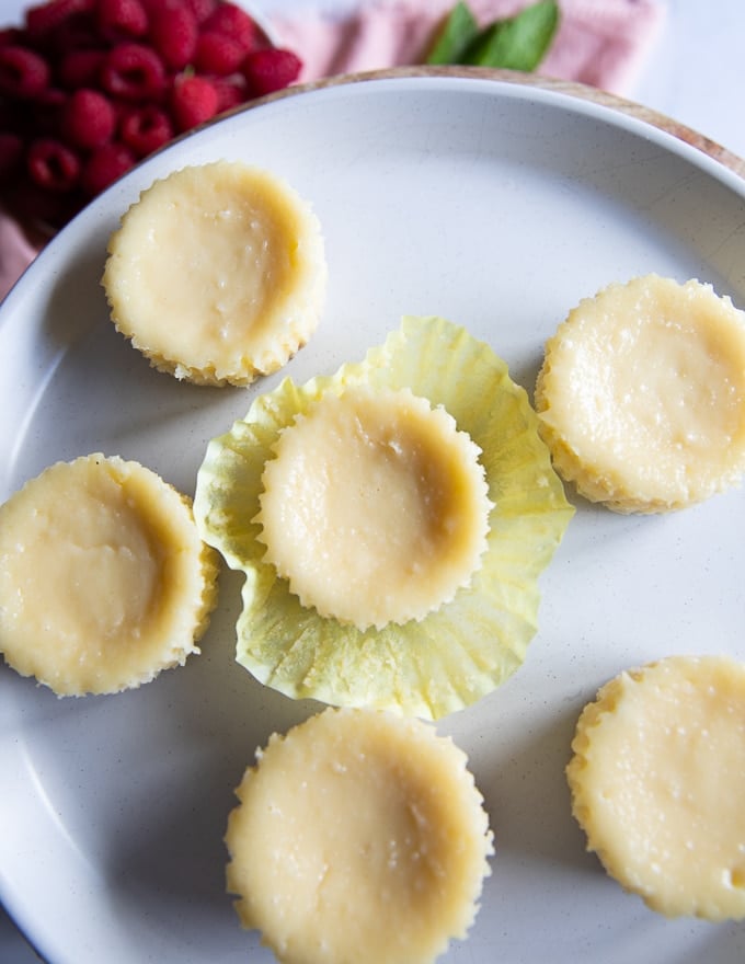 cooled cheesecakes on a plate and a hand peeling off the baking ppers