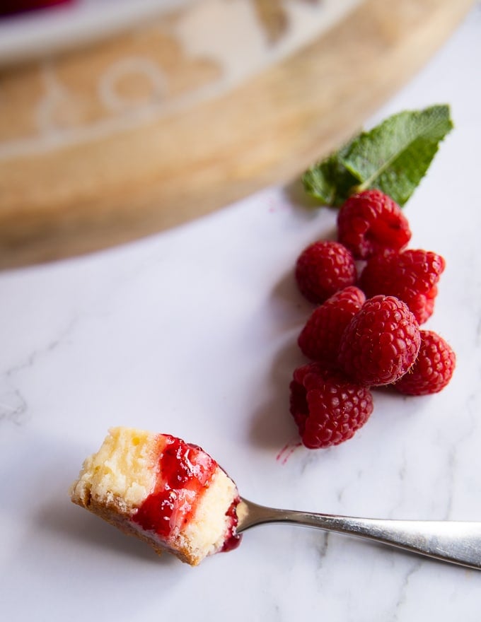 a fork with a bitten piece of cheesecake on a white marble and raspberry sauce