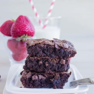 a stack of gluten free brownies recipe on a plate with strawberries and milk