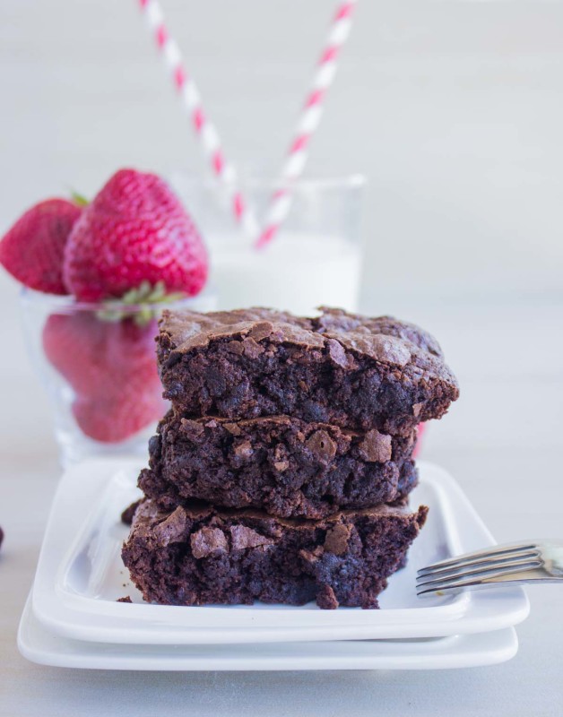 a stack of gluten free brownies recipe on a plate with strawberries and milk