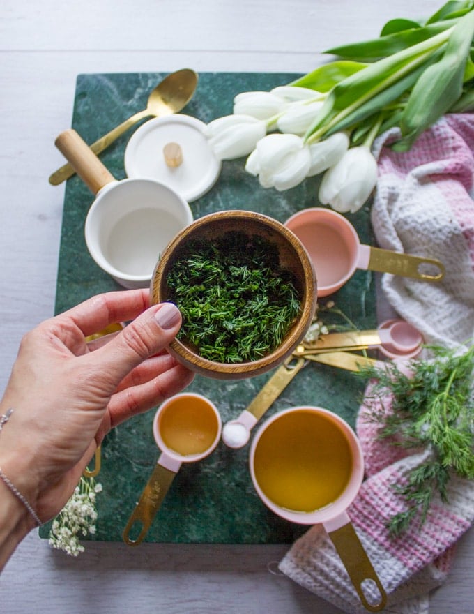 A hand holding a bowl of chopped dill to make the sauce