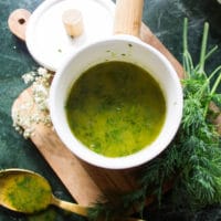 A close up of the dill sauce in a bowl surrounded by fresh dill