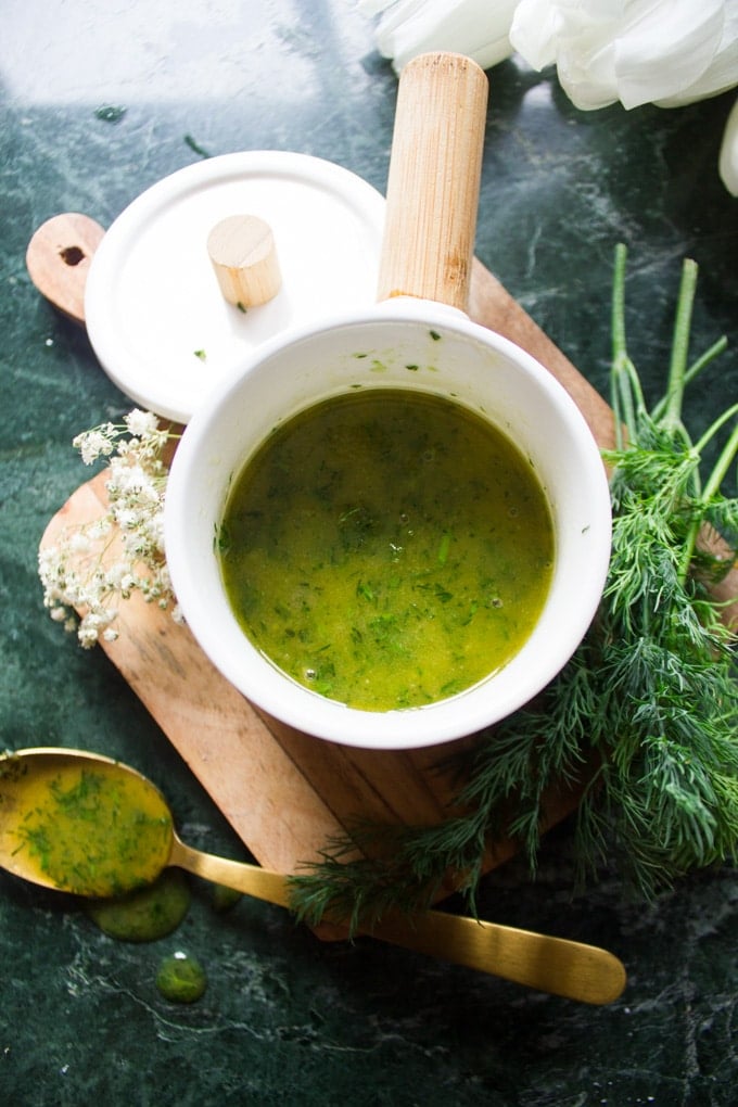 A close up of the dill sauce in a bowl surrounded by fresh dill