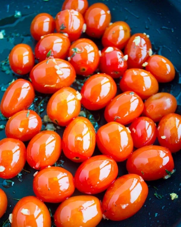 Cocktail tomatoes tossed in a black skillet with some olive oil.