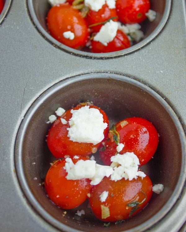 cocktail tomatoes topped with crumbled goat cheese at the bottom of muffin tin molds.