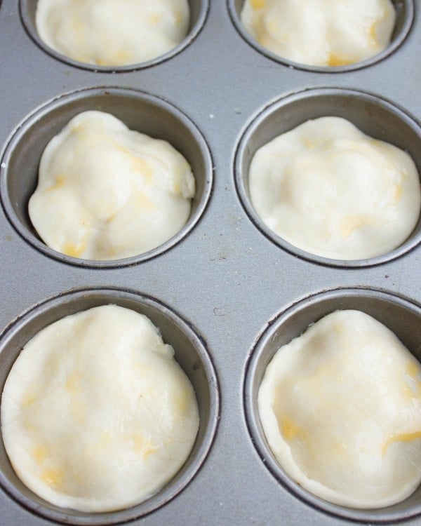 rounds of raw pastry dough placed on top of mini tomatoes for making tarte tatin in a muffins pan.