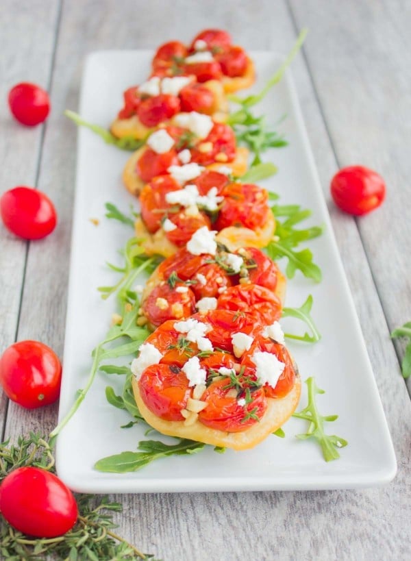 Mini Tomato Tartes Tatin decorated with some arugula and lined up on a while rectangular plate.