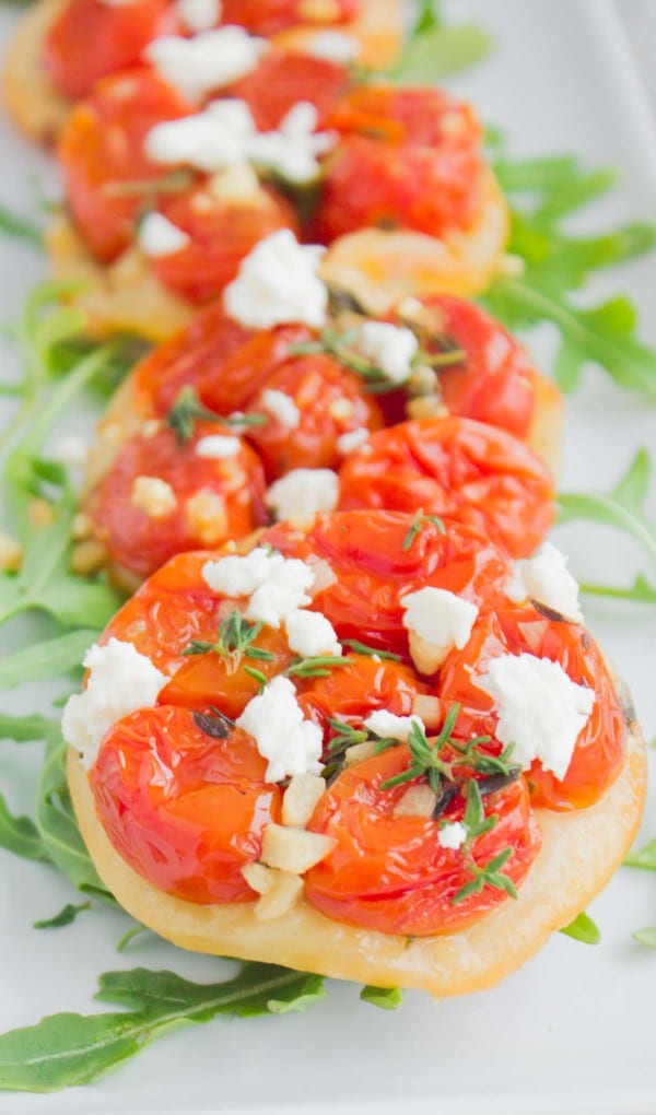 Close-up of Mini Tomato Tartes Tatin decorated with some arugula and lined up on a while rectangular plate 