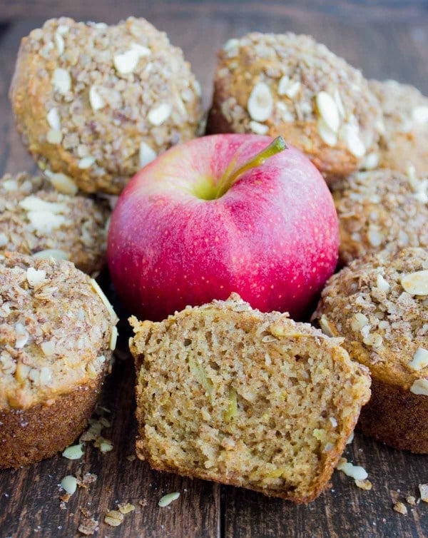 half a Whole Wheat Apple Cinnamon Muffin leaning against a red apple with more muffins in the background