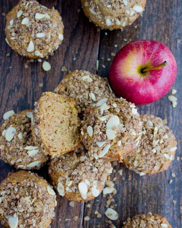 Whole Wheat Apple Cinnamon Muffins with Almond Crumb Topping arranged on a wooden tabletop with an apple in the background