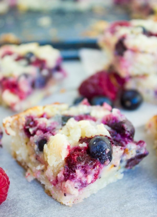 Close-up of cake bars with mixed berries, cream cheese filling and a cookie crumb topping arranged on a baking tray