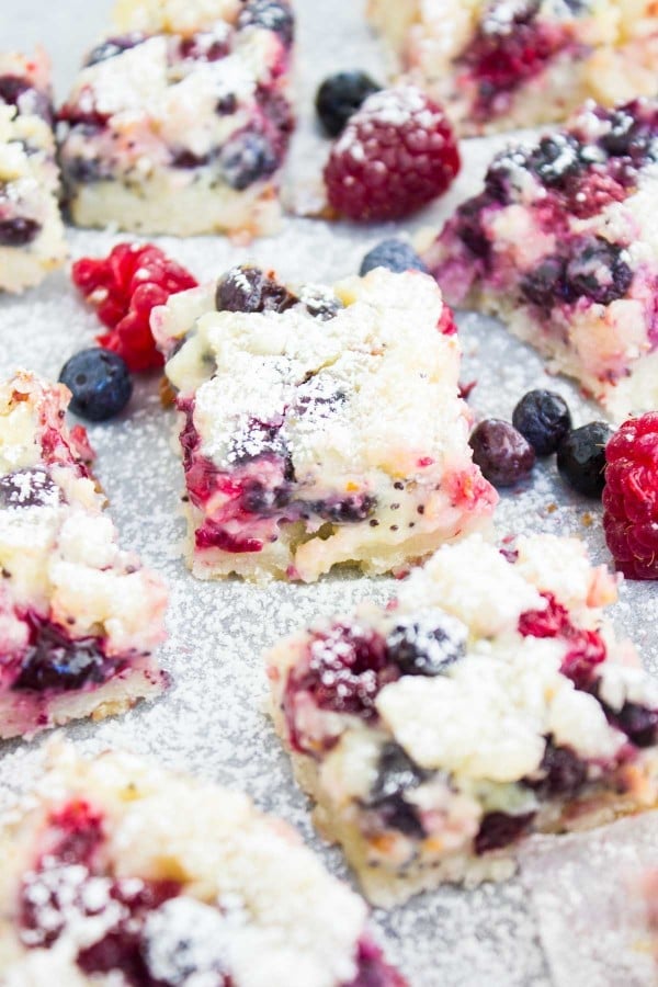 Close-up of sugar-dusted Berry Citrus Poppy Seed Bars with some mixed berries scattered in between