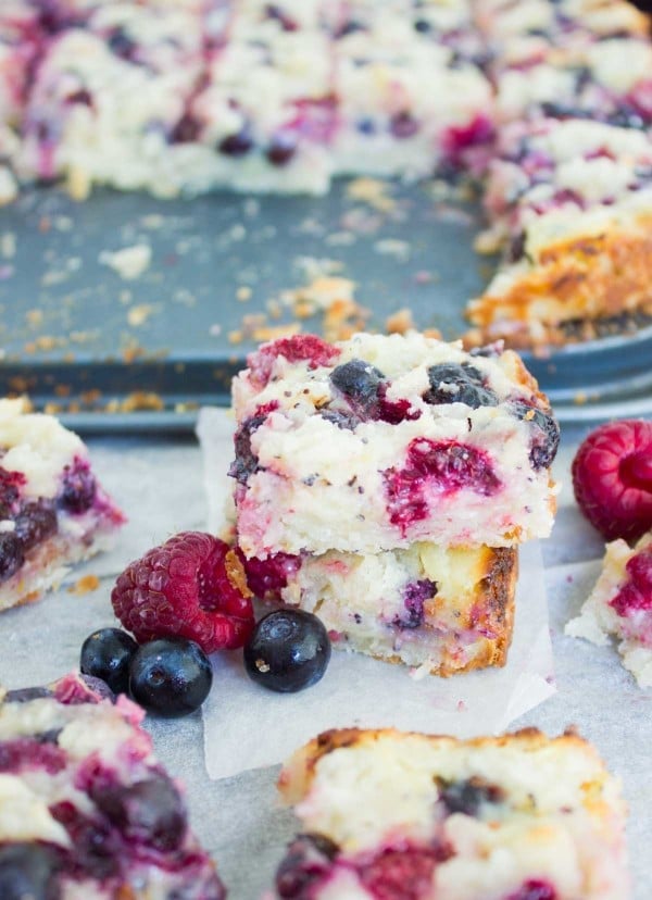Berry Citrus Poppy Seed Bars stacked on top of each other with a sheet pan of cake bars in the background