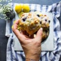 A hand holding a glazed drop biscuits with blueberries and lemon over a plate of drop biscuits