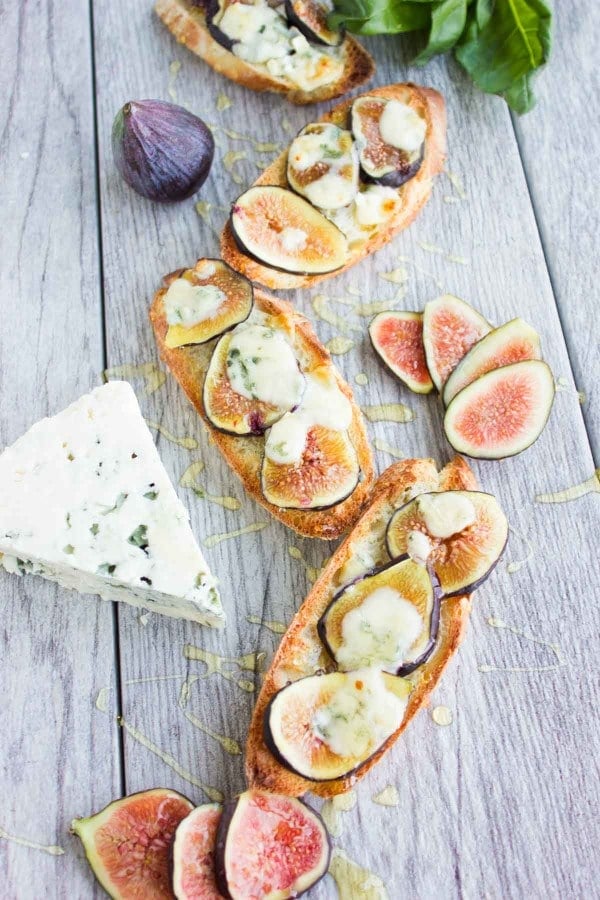 Fig Blue Cheese Honey Crostini drizzled with honey, served on a rustic table with a wedge of blue cheese and some figs in the background - crostini recipe