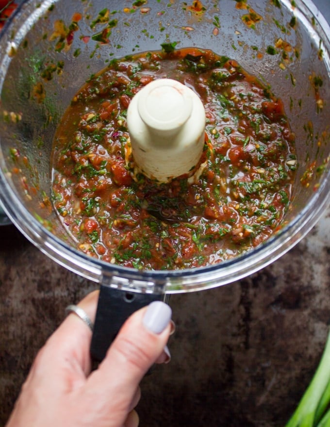 a hand holding the bowl of a food processor after pulsing a few times showing homemade salsa