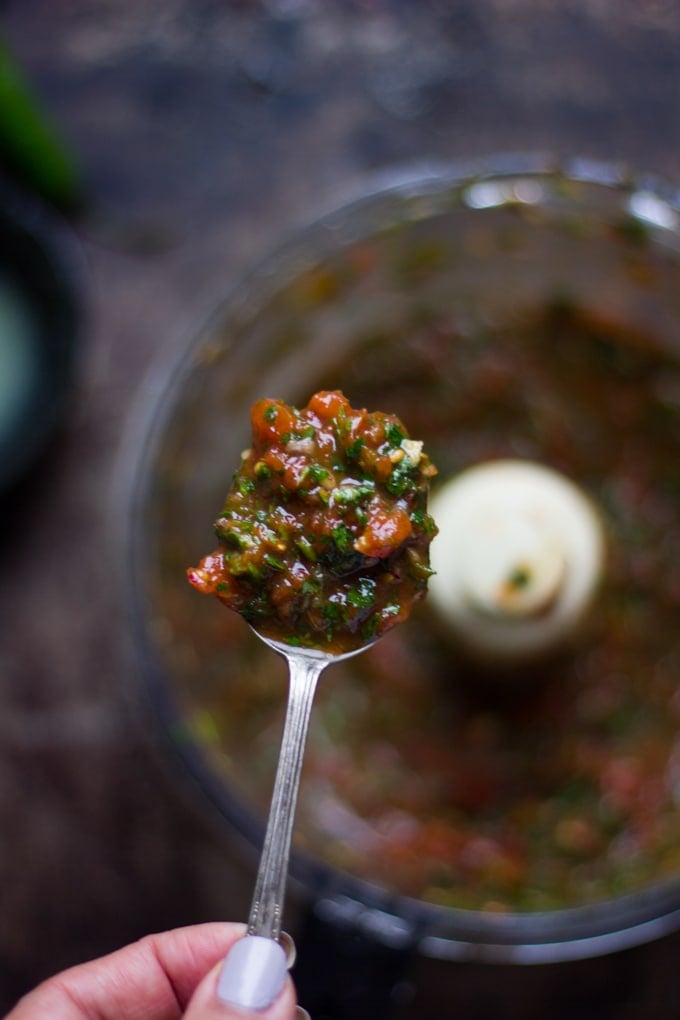 a spoon of the salsa recipe over the bowl of salsa checking consistency to add more tomato juice or not