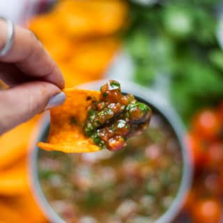 A hand holding a chip dipped in homemade salsa showing the texture