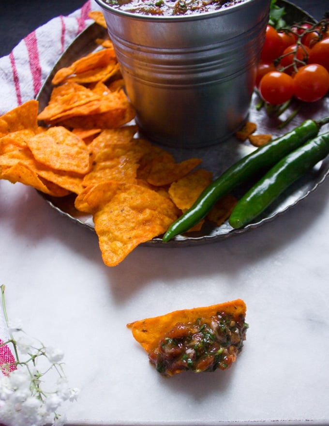 A chip dipped in salsa over a white marble sowing the texture