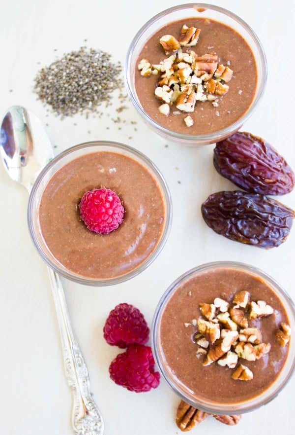 Instant Chia Puddings in three glasses with chia seeds, dates and raspberries on the side