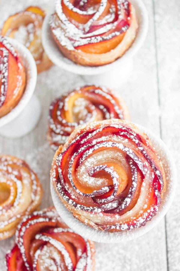 Bite sized Peach Plum Rose Tarts dusted with icing sugar served on a rustic table