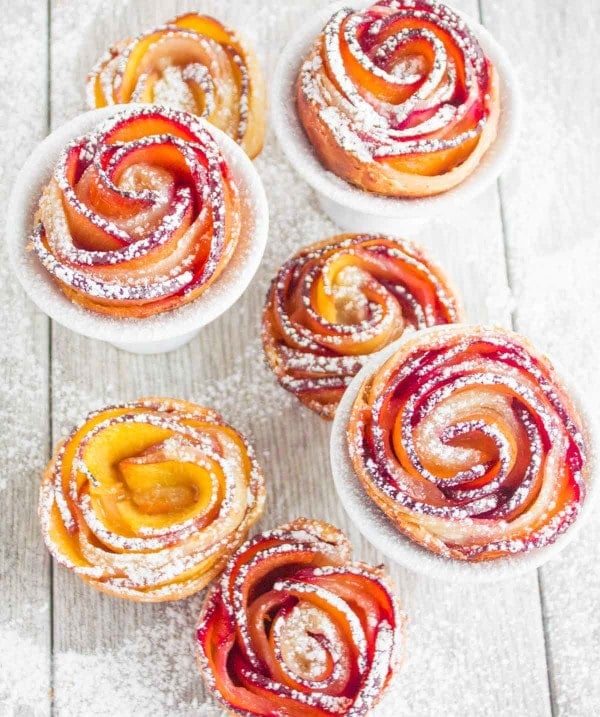 Peach Plum Rose Tarts dusted with icing sugar on a rustic table