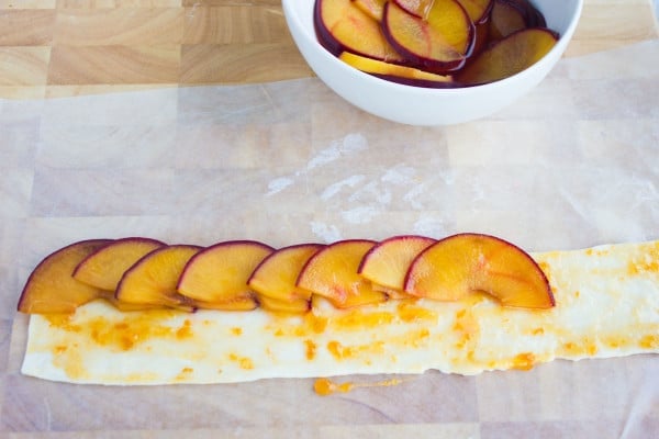 a jam covered strip of pastry being topped with sliced plums to make rose tarts