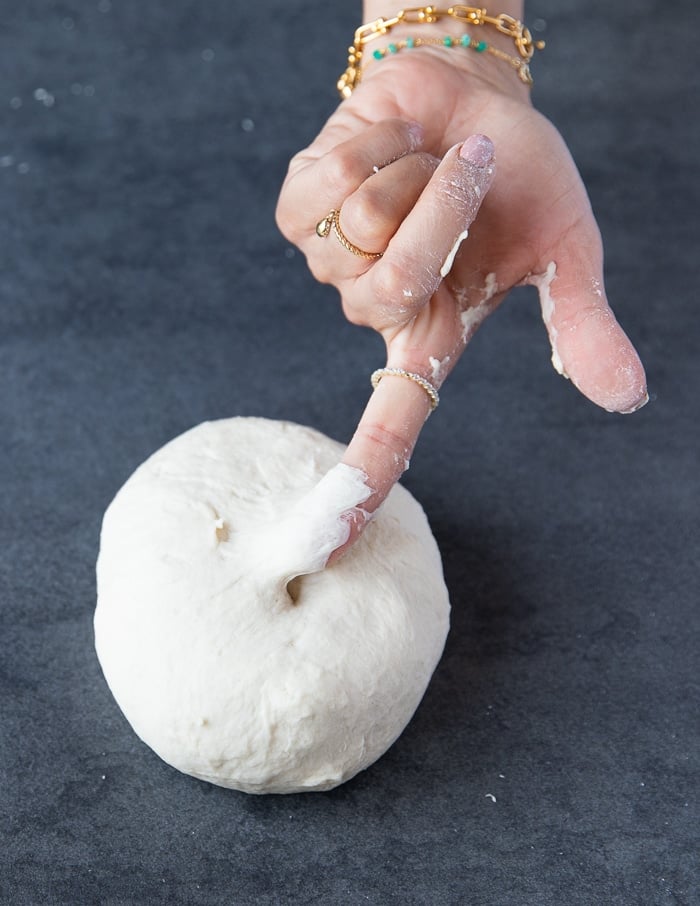 A finger sticking sliughtly to the dough showing the correct consistency to pizza dough recipe