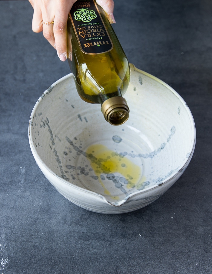 A hand pouring olive oil into the bowl for the pizza dough to rise