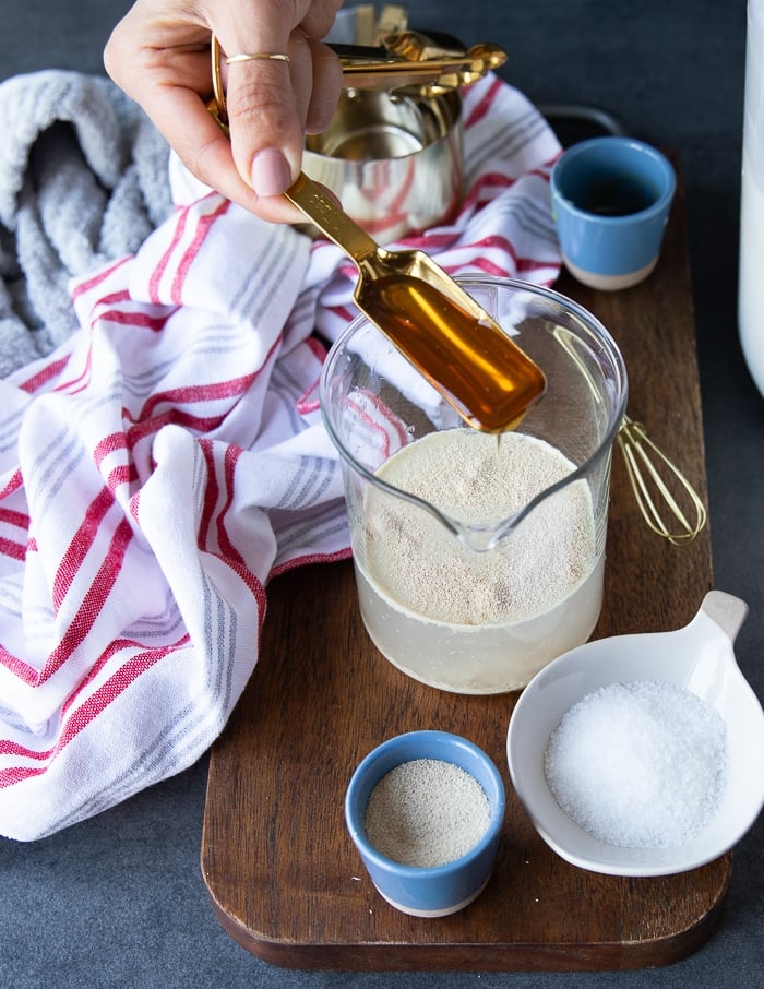 Pouring honey into a cup with warm water and yeast to proof the yeast.