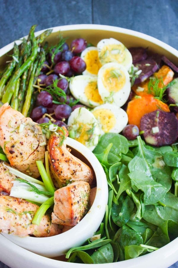 Close-up of Salmon Asparagus Sweet Potato Nicoise Salad arranged in a big salad bowl and topped with sweet potatoes grapes, boiled eggs and broiled salmon and asparagus