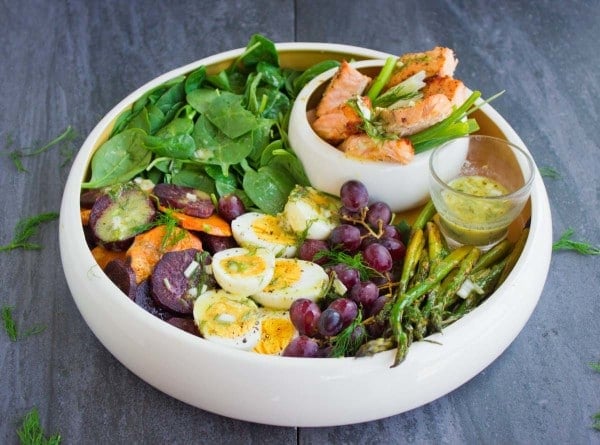 Salmon Asparagus Sweet Potato Nicoise Salad served in a big salad bowl with 2 little side dishes with dressing and broiled salmon nestled in between the ingredients