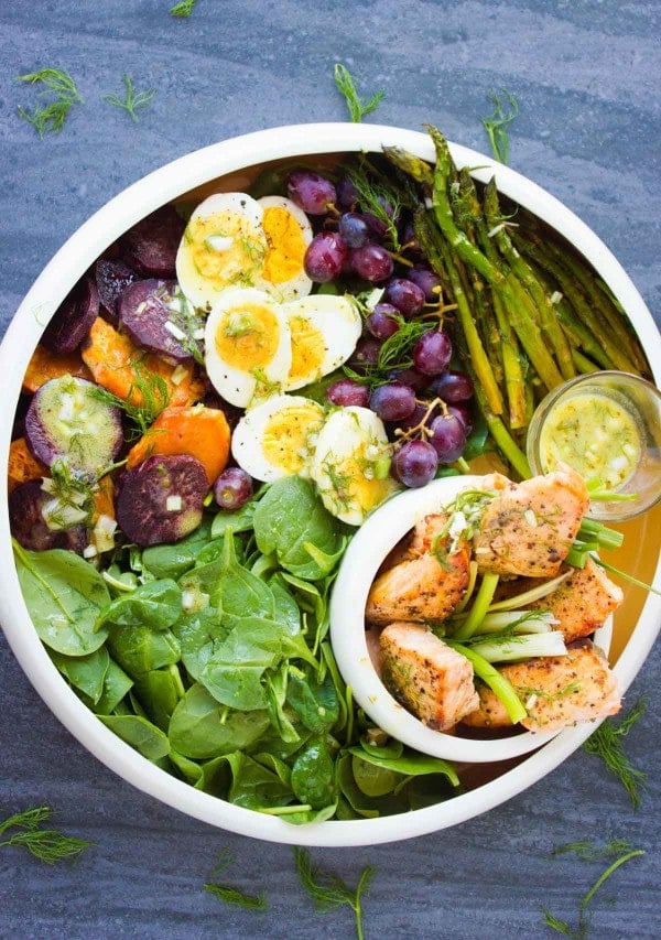 Salmon Asparagus Sweet Potato Nicoise Salad arranged in a big salad bowl and topped with sweet potatoes grapes, boiled eggs and broiled salmon and asparagus