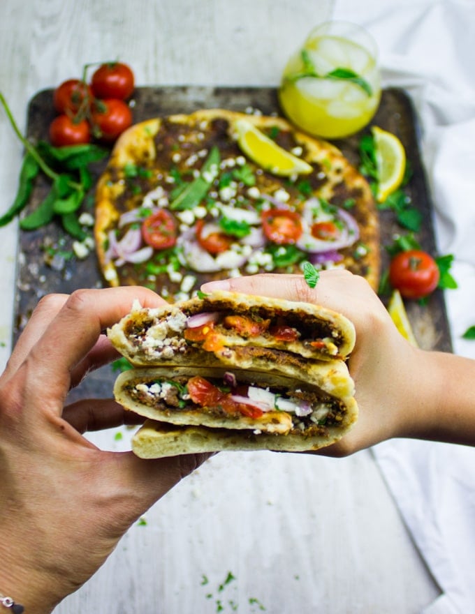 two hands holding a rolled up lahmacun pizza 