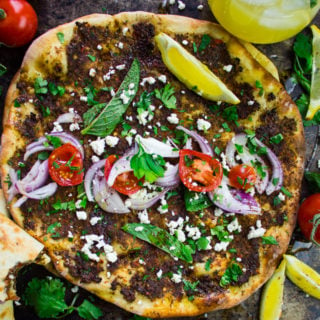 close up of a turkish piza lahmacun topped with herbs, tomatoes, onions, lemon slices and feta cheese