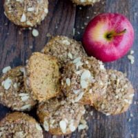 Whole Wheat Apple Cinnamon Muffins with Almond Crumb Topping arranged on a wooden tabletop with an apple in the background