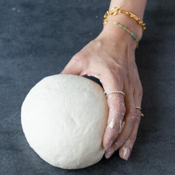Holding pizza dough in the left hand.