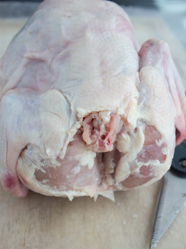 a whole chicken, uncooked on a cutting board ready to be butterflied