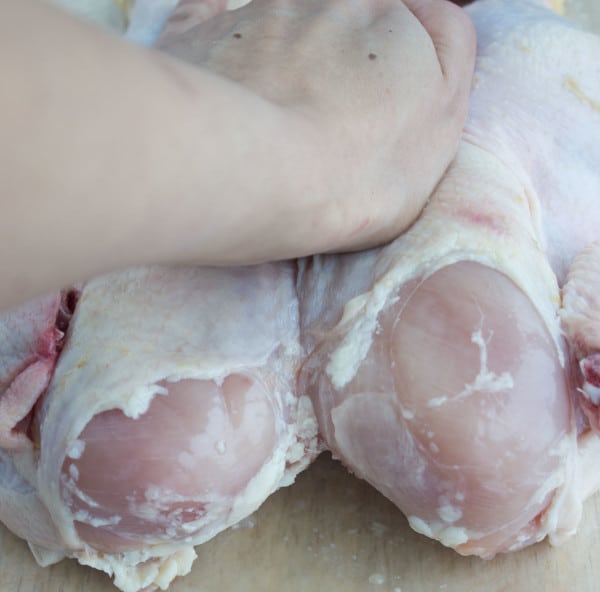 the breast bone of a whole chicken being broken to butterfly it